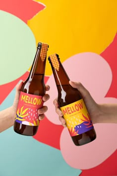 two people holding beer bottles in front of a colorful background