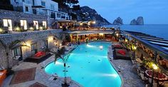 an outdoor swimming pool surrounded by stone buildings and water features lit up at night time