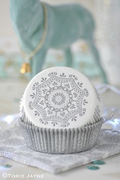 a white cupcake sitting on top of a doily next to an elephant figurine