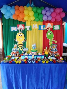 a table topped with lots of colorful balloons and desserts next to a blue tent