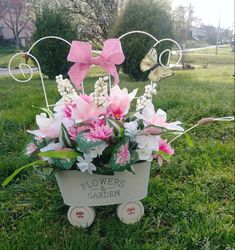 a flower pot with pink and white flowers in it on top of a wheelbarrow