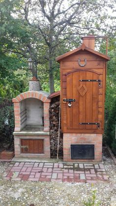 an outdoor wood fired oven in the middle of a brick area with trees and bushes behind it