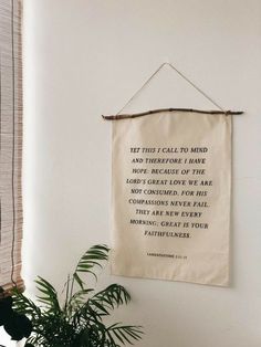 a wall hanging with a bible verse on it next to a potted plant and window