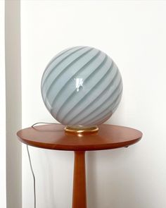 a lamp sitting on top of a wooden table next to a white wall and floor