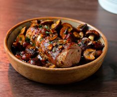 a bowl filled with meat and mushrooms on top of a wooden table next to a cup