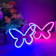 two butterfly shaped neon signs sitting on top of a table next to a potted plant