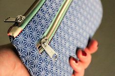 a woman's hand holding a blue and white purse with two zippers on it