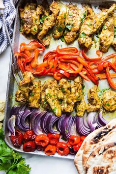 a tray filled with meat and vegetables on top of a table next to pita bread