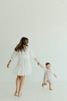 a woman holding the hand of a small child as they walk across a white floor