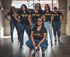 a group of women standing next to each other in front of a building wearing black shirts