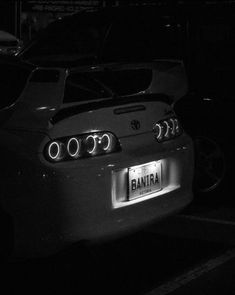 the back end of a white car parked in a parking lot at night with its lights on