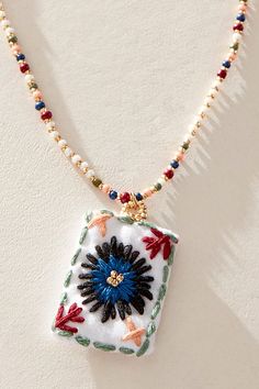 a white necklace with a blue and red flower in the center on a beaded chain