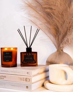 two candles sitting next to each other on top of books and a vase filled with feathers