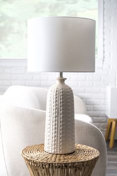 a white table lamp sitting on top of a wicker basket next to a couch