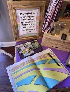 an open book sitting on top of a purple table next to a wooden frame with pictures