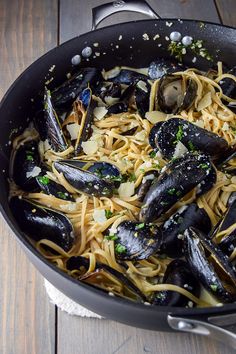 a pan filled with pasta and mussels on top of a wooden table