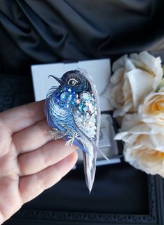 a small bird sitting on top of a person's hand next to some flowers