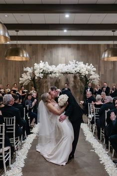 a bride and groom kissing in front of an aisle with white flowers on the side