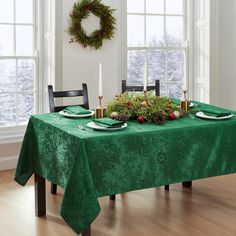 the table is set for christmas dinner with green linens and greenery on it