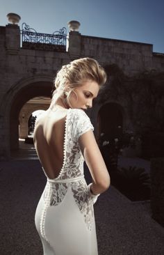 a woman in a white dress is standing near a building and looking down at the ground