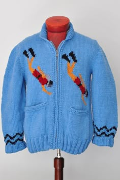 a blue knitted jacket with an orange fish on the front and black, red, and yellow design on the back