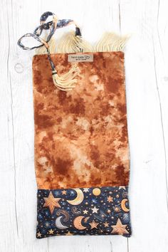 a brown and blue bag with stars, moon and tassels on it sitting on a white wooden surface