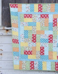 a patchwork quilt hanging on the side of a wooden building with an old door in the background