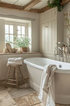 a white bath tub sitting under a window next to a wooden stool and counter top