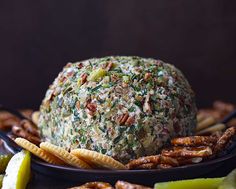 a cheese ball covered in nuts and herbs on a plate with crackers next to it