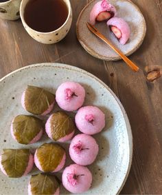 there are some pink donuts on the plate next to a cup of tea and spoons