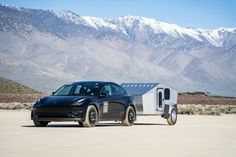 a black car parked in the desert with mountains in the background