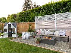 an outdoor living area with couches, fire pit and dog house in the background