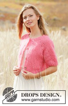 a woman standing in tall grass wearing a pink sweater