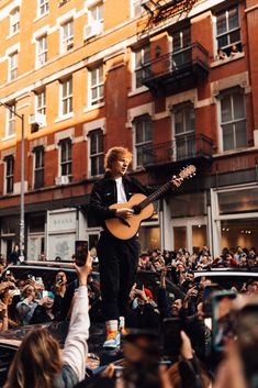 a man standing on top of a stage holding a guitar in front of a crowd