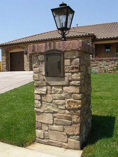 a stone mailbox in front of a house with a light on it's top