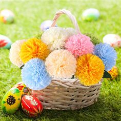 an easter basket filled with pom poms and colorful eggs on the green grass