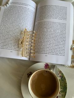 a cup of coffee and an open book on a table with pearls, beads and necklaces