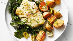 a white plate topped with fish, potatoes and green vegetables on top of a table