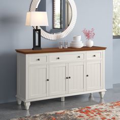 a white dresser with a mirror on top and a lamp next to it in front of a blue wall