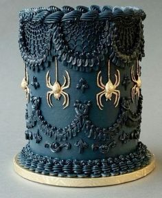 a blue cake with gold decorations and spider webs on the top, sitting on a plate