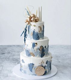 a three tiered blue and white cake with gold decorations on the top, sitting on a plate