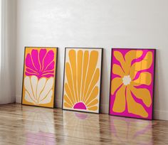 three framed art pieces on a wooden floor in front of a white wall and window