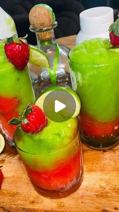 two glasses filled with liquid and strawberries on top of a wooden table next to bottles