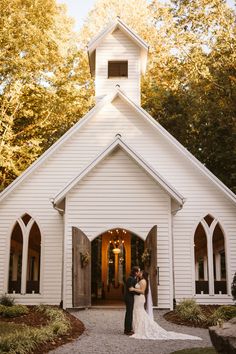 a bride and groom standing in front of a white church with lights on it's steeple