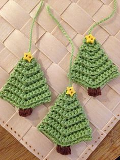 two crocheted christmas trees hanging from strings on a woven tablecloth with yellow stars