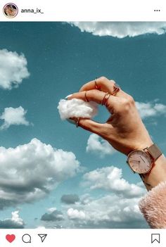 a person holding cotton in their hand under a blue sky with white clouds and a watch