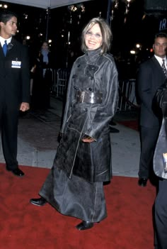 a woman in a black coat and tie standing on a red carpet with other people