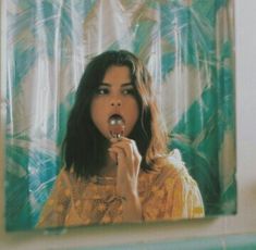 a young woman brushing her teeth in front of a mirror with blue and green curtains