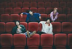 three men sitting in the middle of a movie theater with red seats and one man holding a drink