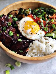 a wooden bowl filled with rice, meat and veggies next to an egg